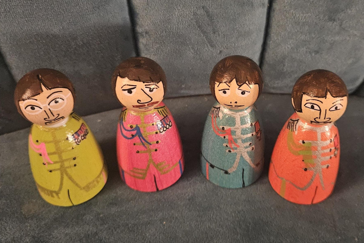 Four wooden peg dolls with colorful clothing on a dark fabric background