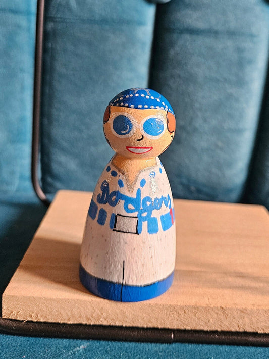 Wooden peg doll with blue accents on a wooden stand against a blue cushioned background